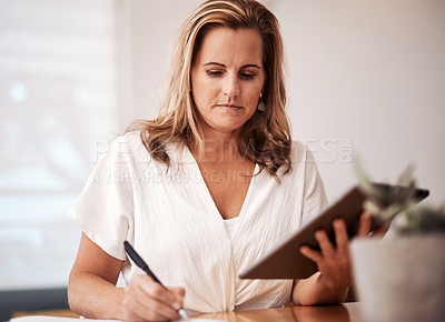 Buy stock photo Shot of a mature businesswoman writing notes while using a digital tablet in an office