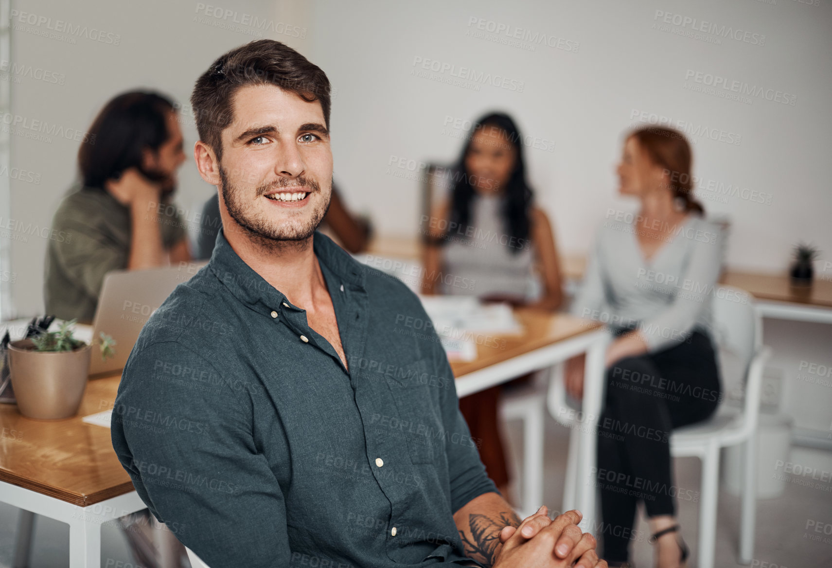 Buy stock photo Portrait of a young businessman sitting in an office with his colleagues in the background