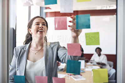 Buy stock photo Shot of a young businesswoman brainstorming with notes on a glass wall during a presentation with her colleagues in an office