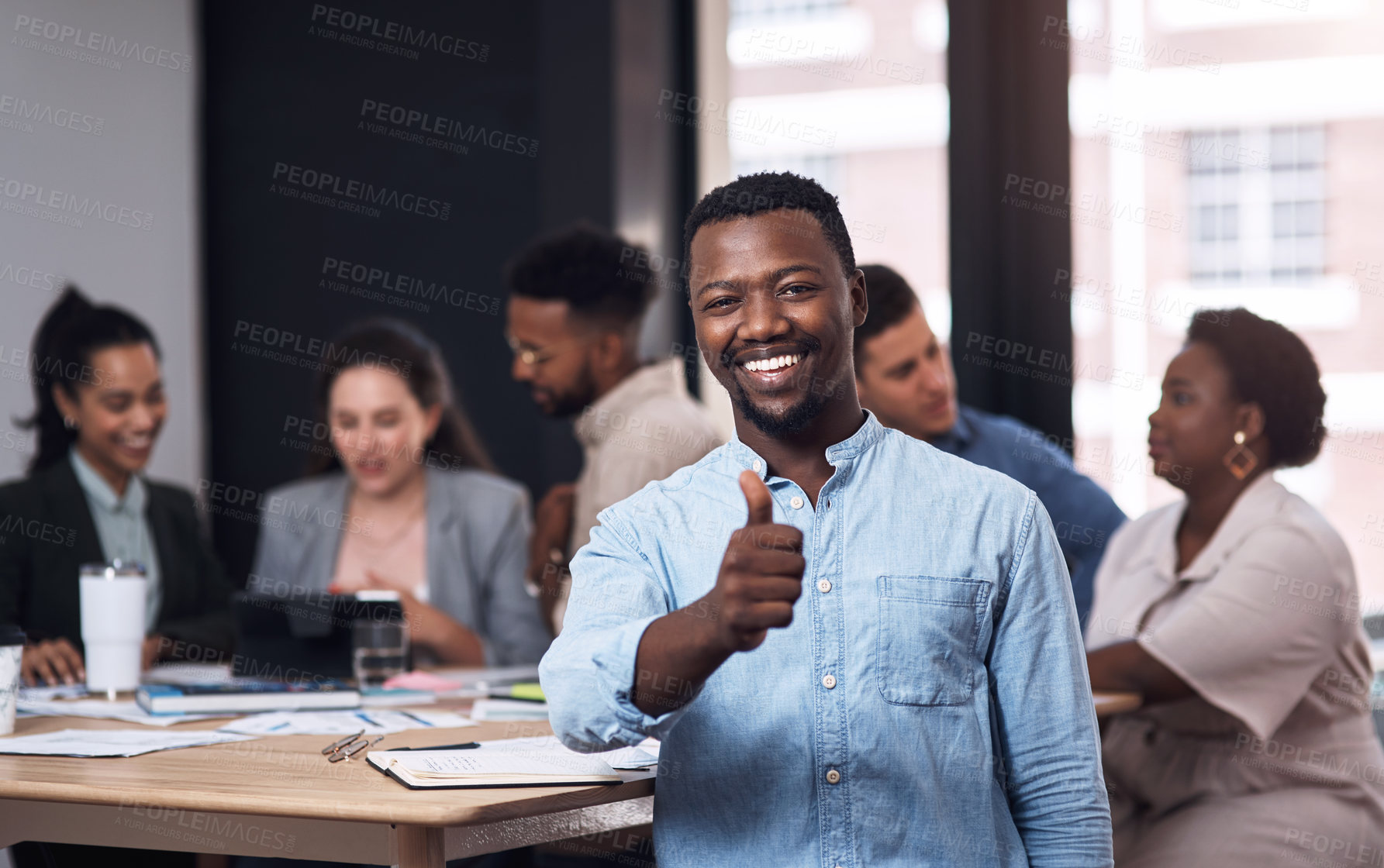Buy stock photo Portrait of a young businessman showing thumbs up in an office with his colleagues in the background