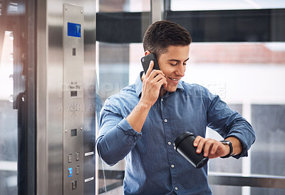 Buy stock photo Shot of a young businessman talking on a cellphone and checking his watch while standing in an elevator