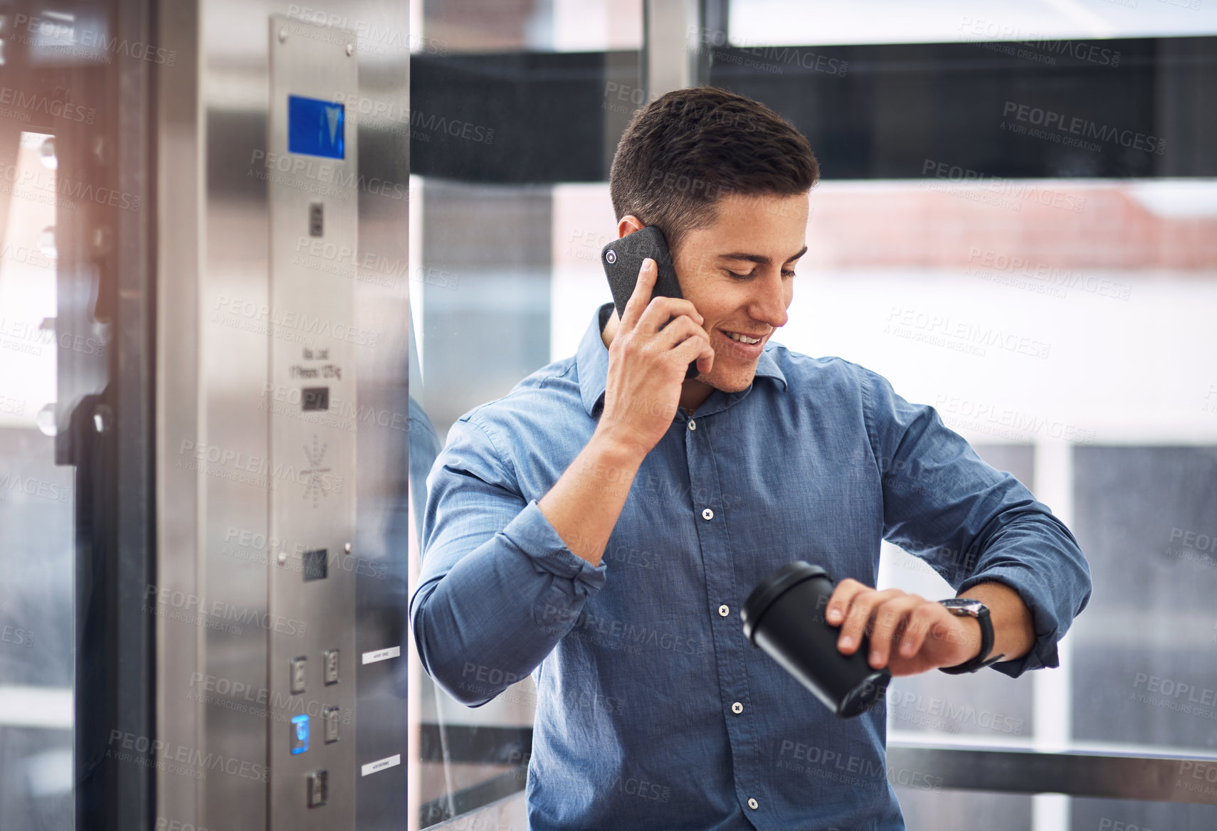 Buy stock photo Shot of a young businessman talking on a cellphone and checking his watch while standing in an elevator