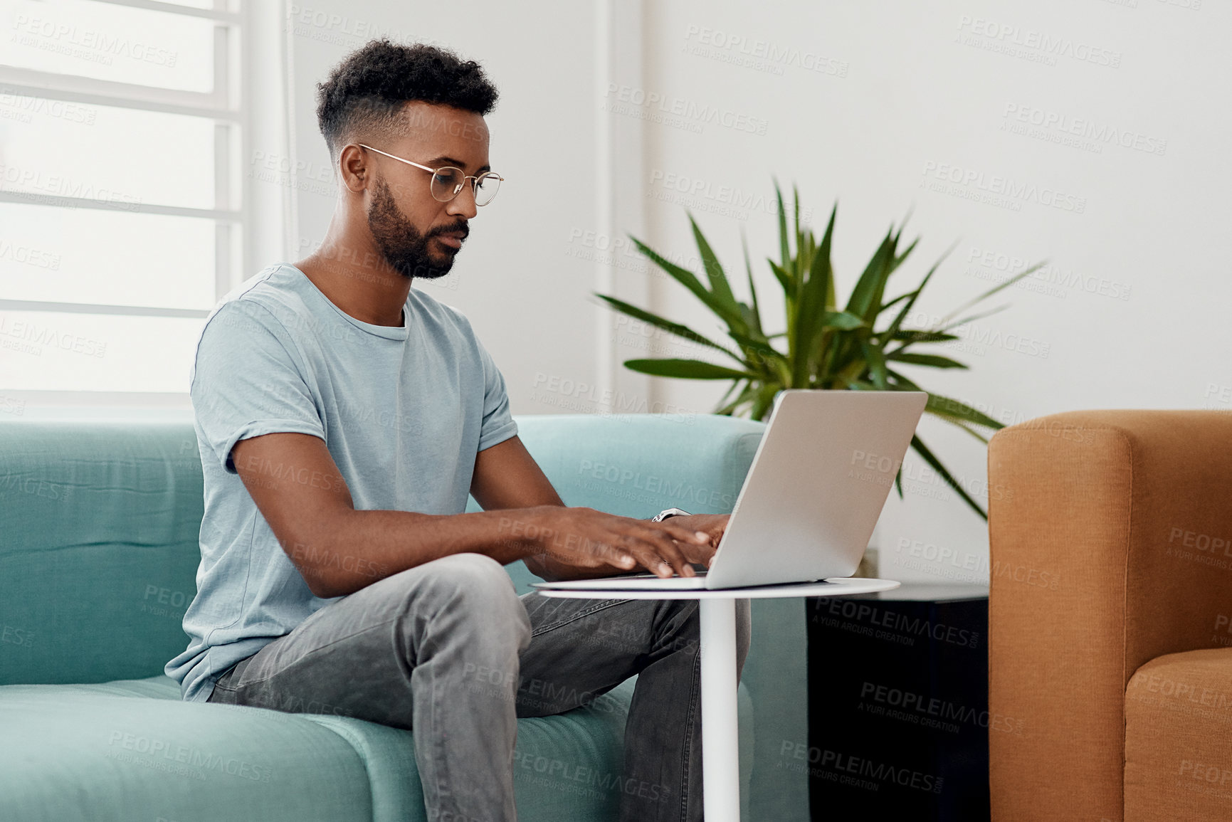 Buy stock photo Cropped shot of a handsome young businessman sitting alone and using his laptop in the office