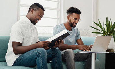 Buy stock photo Cropped shot of two handsome businessmen sitting together and reading paperwork while using a laptop in the office