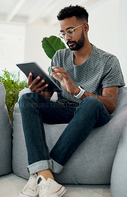 Buy stock photo Cropped shot of a handsome young businessman sitting alone and using his tablet in the office
