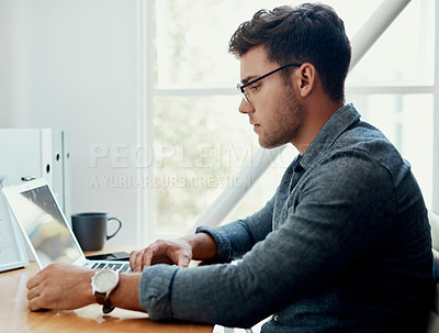 Buy stock photo Cropped shot of a handsome young businessman sitting alone and using his laptop in the office
