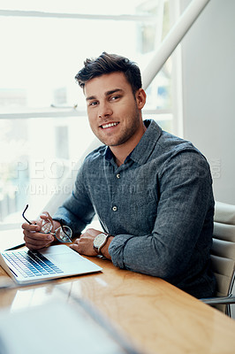Buy stock photo Cropped portrait of a handsome young businessman sitting alone and using his laptop in the office