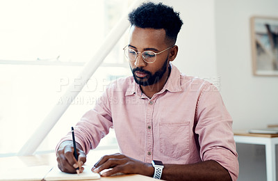 Buy stock photo Cropped shot of a handsome young businessman sitting and writing in a notebook while in the office alone