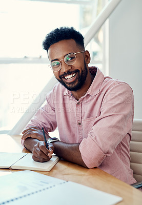 Buy stock photo Cropped portrait of a handsome young businessman sitting and writing in a notebook while in the office alone