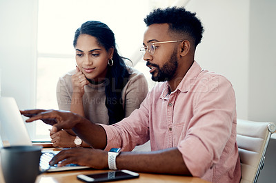 Buy stock photo Cropped shot of two young businesspeople sitting in the office and working on a laptop together