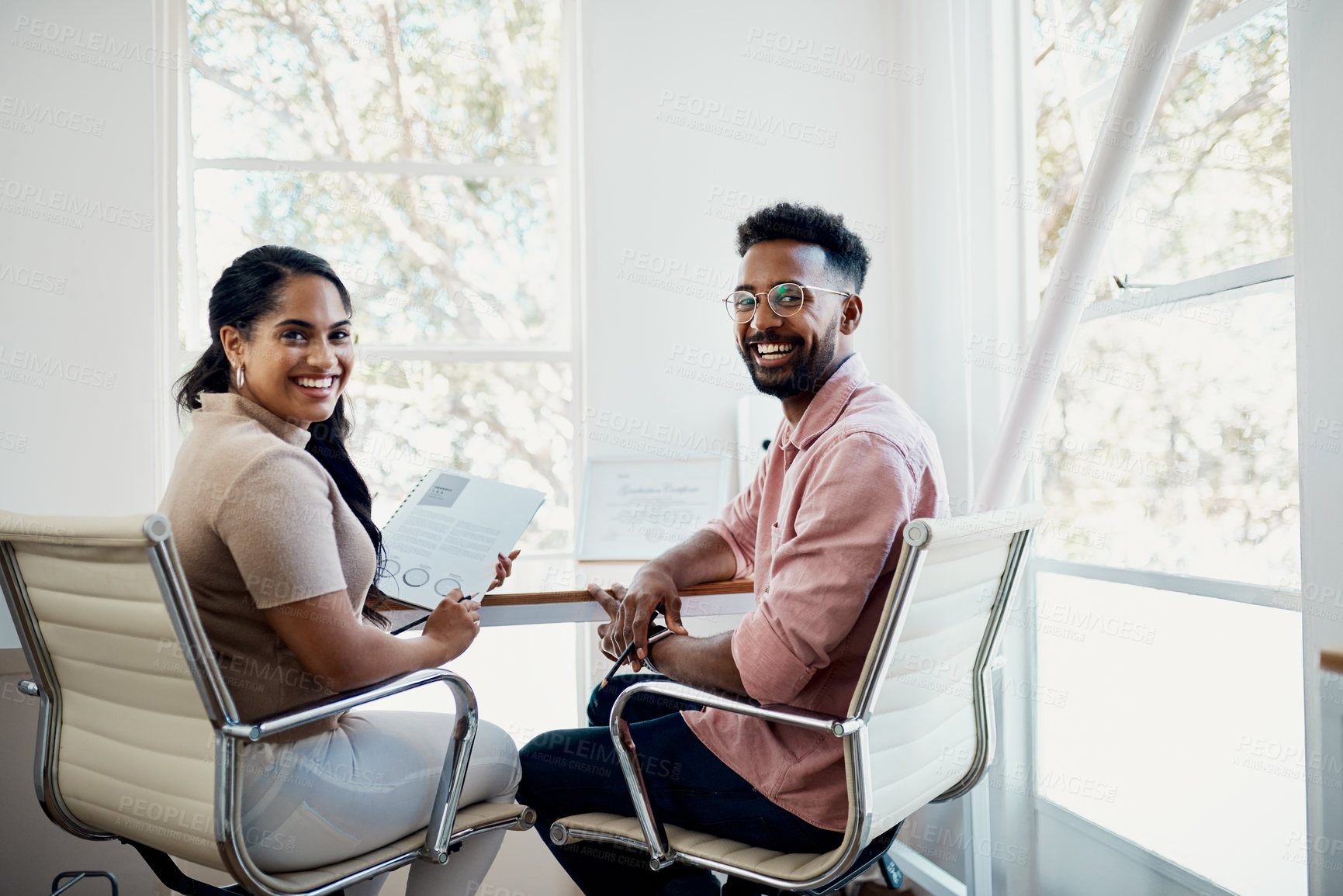 Buy stock photo Cropped portrait of two young businesspeople sitting together in the office and going through paperwork