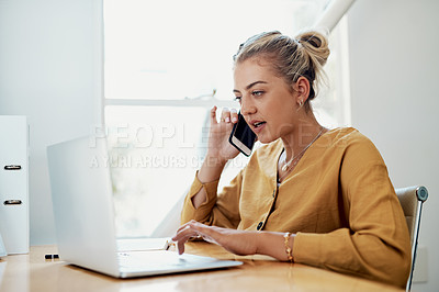 Buy stock photo Cropped shot of an attractive young businesswoman sitting and using her cellphone while working on a laptop in the office