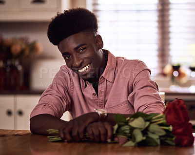 Buy stock photo Cropped portrait of a handsome romantic young man smiling while holding a bunch of roses in his kitchen at home