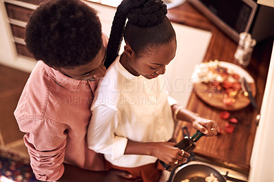 Buy stock photo High angle shot of an affectionate young man hugging his wife while she's cooking in their kitchen at home
