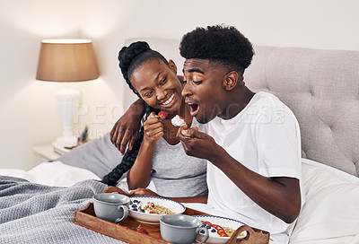 Buy stock photo Shot of a happy young couple enjoying breakfast in bed together