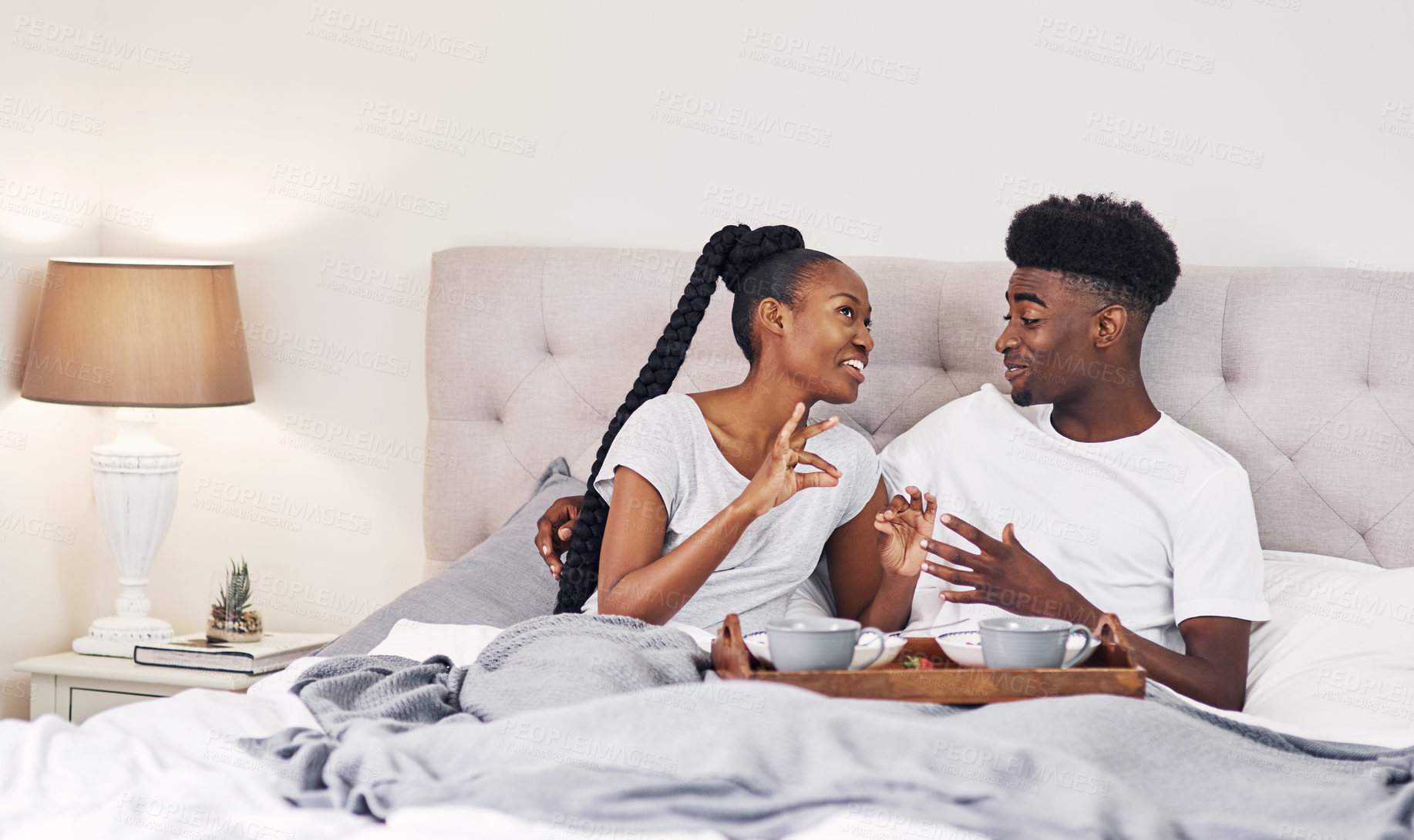 Buy stock photo Shot of a happy young couple enjoying breakfast in bed together