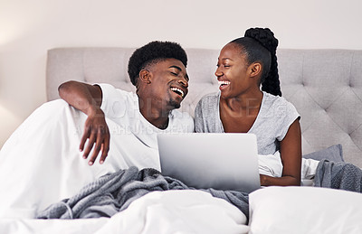 Buy stock photo Shot of a young couple using a laptop while relaxing on their bed