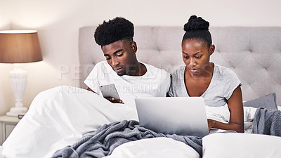 Buy stock photo Shot of a young couple using wireless devices while sitting on their bed together