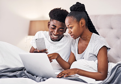 Buy stock photo Shot of a young couple using wireless devices while sitting on their bed together