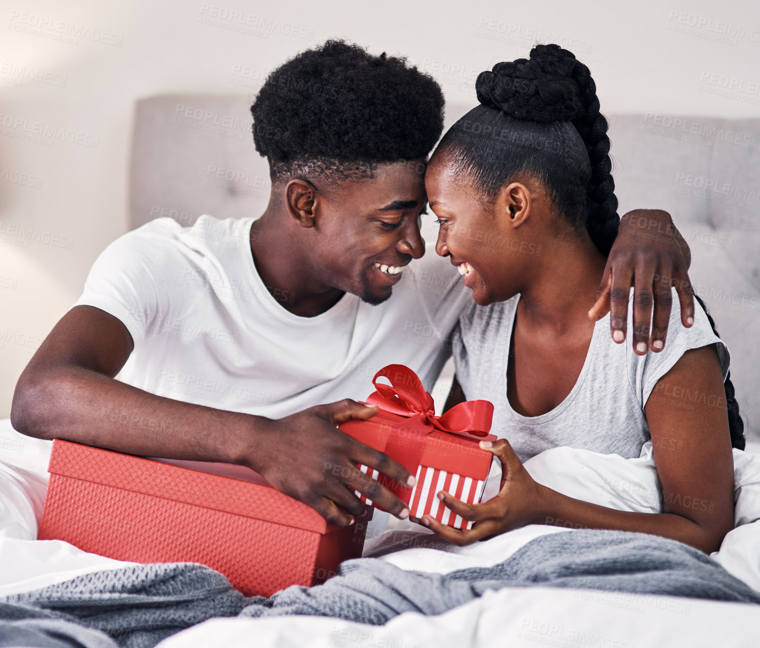 Buy stock photo Shot of a young couple exchanging gifts while sitting on their bed