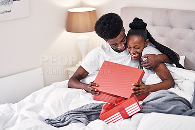 Buy stock photo Shot of a young man spoiling his girlfriend with gifts in their bedroom