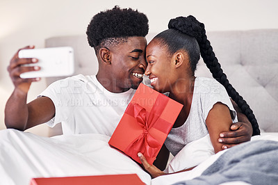 Buy stock photo Shot of a young woman holding up a gift box while taking a selfie with her boyfriend