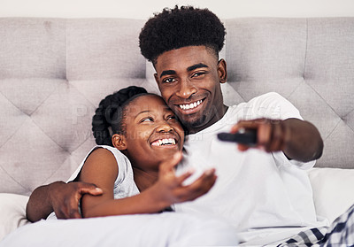 Buy stock photo Shot of a young man using a remote control while lying in bed with his girlfriend