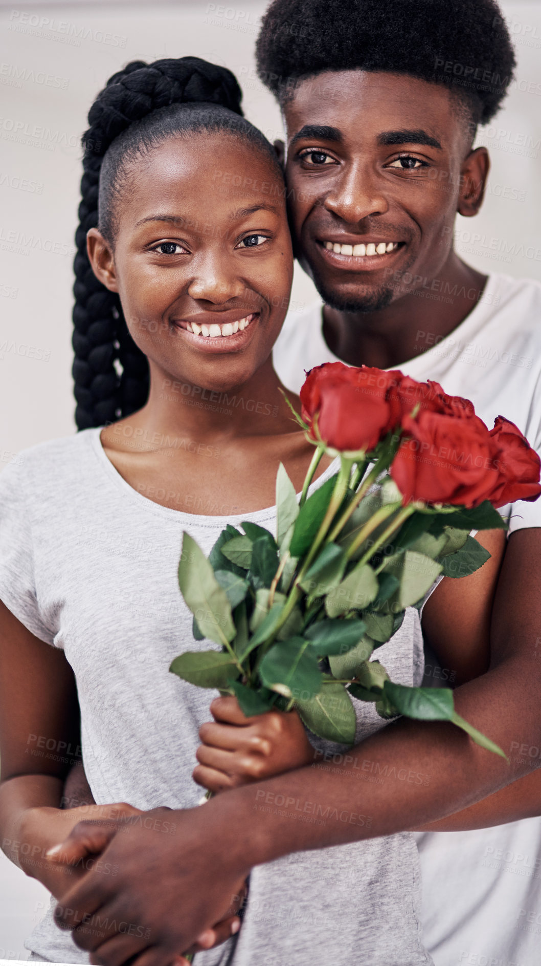 Buy stock photo Shot of a young woman holding a bunch of red roses while standing with her boyfriend at home