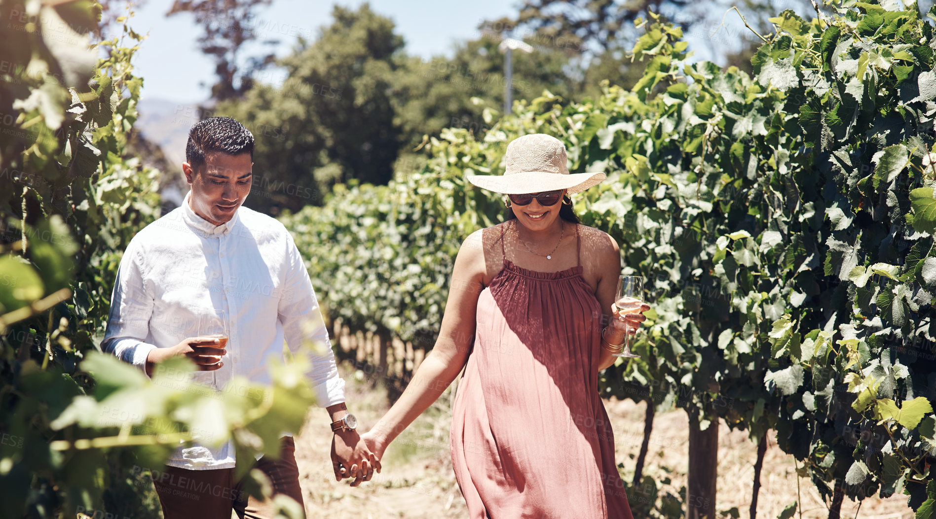 Buy stock photo Shot of a young couple having a glass of wine while walking through a vineyard