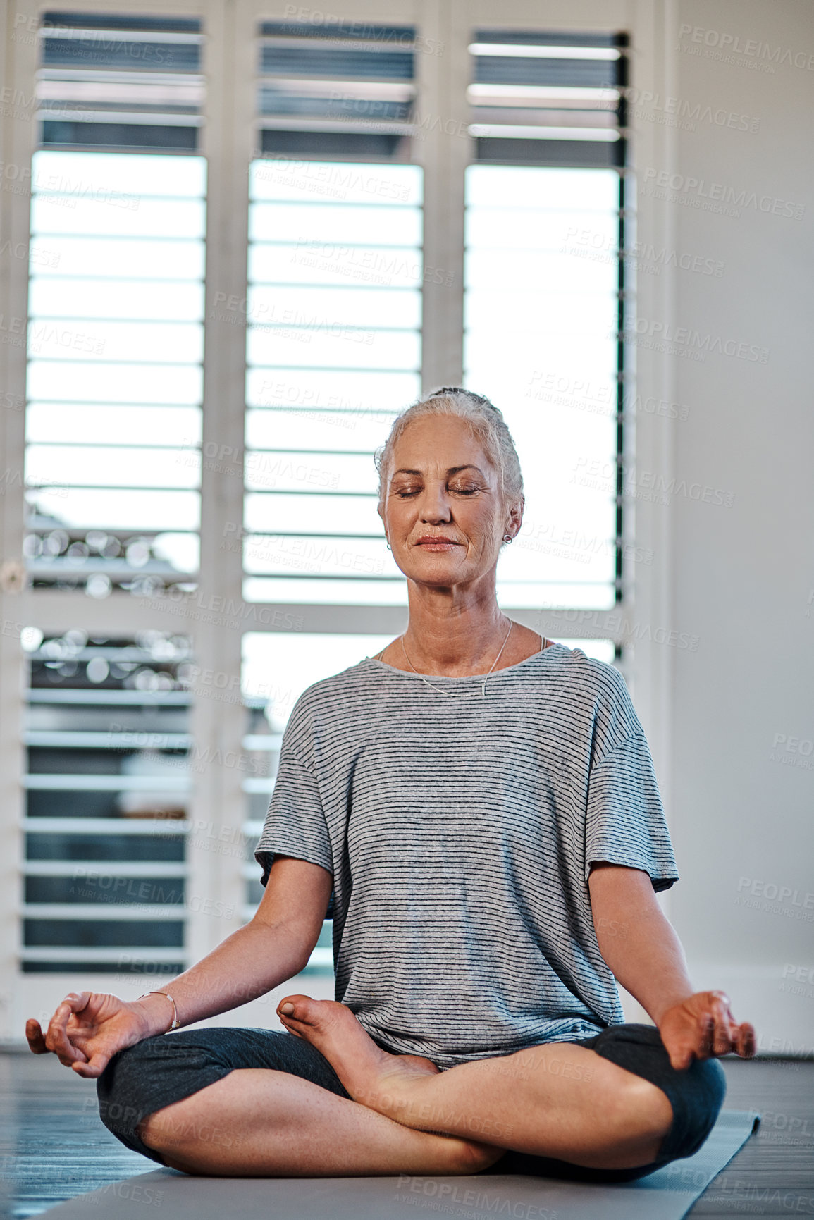 Buy stock photo Shot of a cheerful mature woman practicing yoga while meditating inside of a studio during the day
