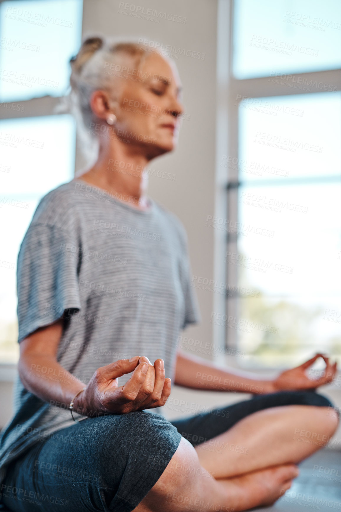Buy stock photo Shot of a cheerful mature woman practicing yoga while meditating inside of a studio during the day