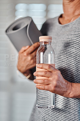 Buy stock photo Cropped shot of an unrecognizable mature woman holding a bottle of water and yoga mat ready to start her morning session of yoga inside of a studio