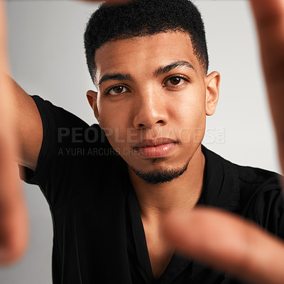 Buy stock photo Portrait of a handsome young man making a frame with his fingers while standing against a grey background inside of a studio