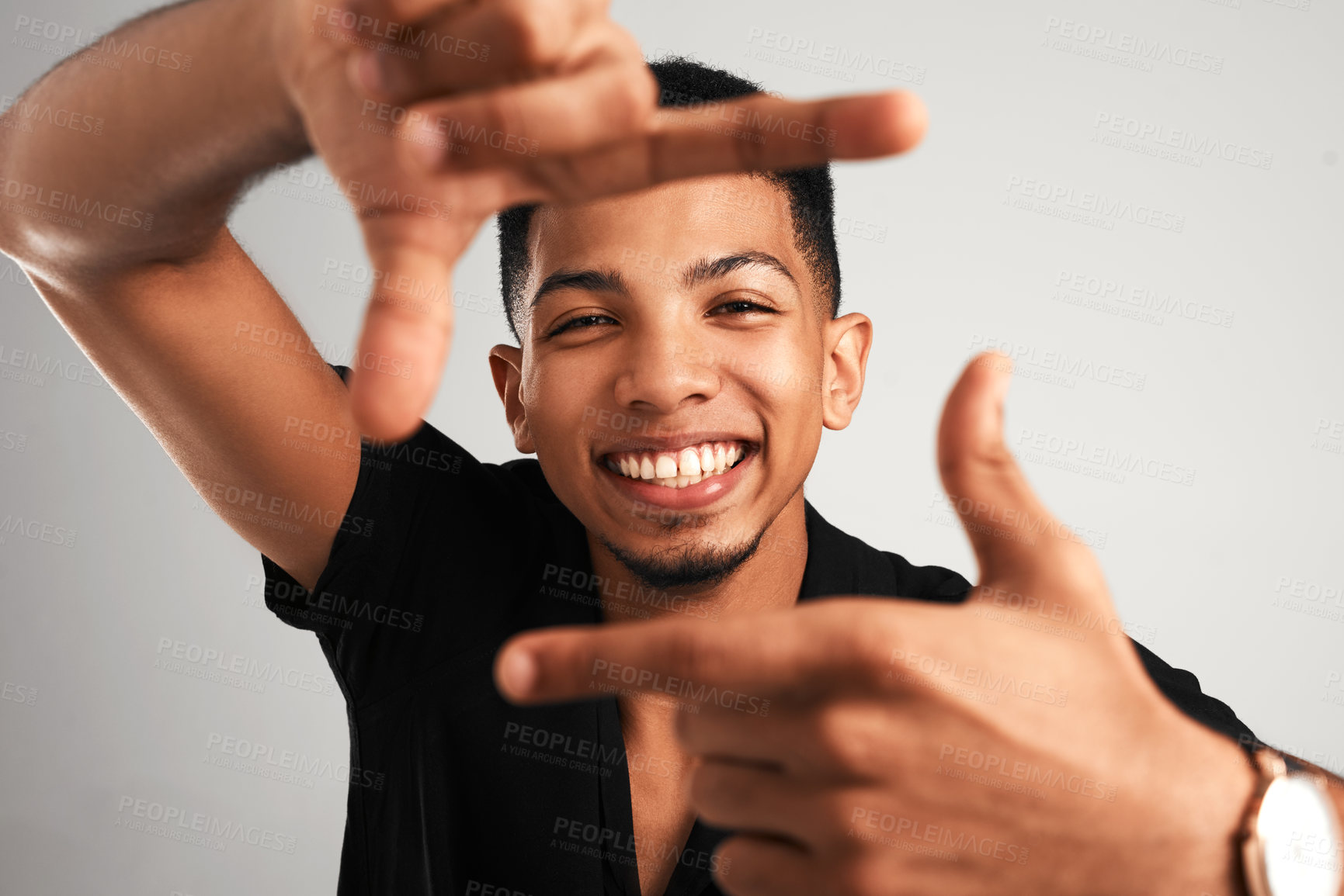 Buy stock photo Portrait of a cheerful young man making a frame with his fingers while standing against a grey background inside of a studio
