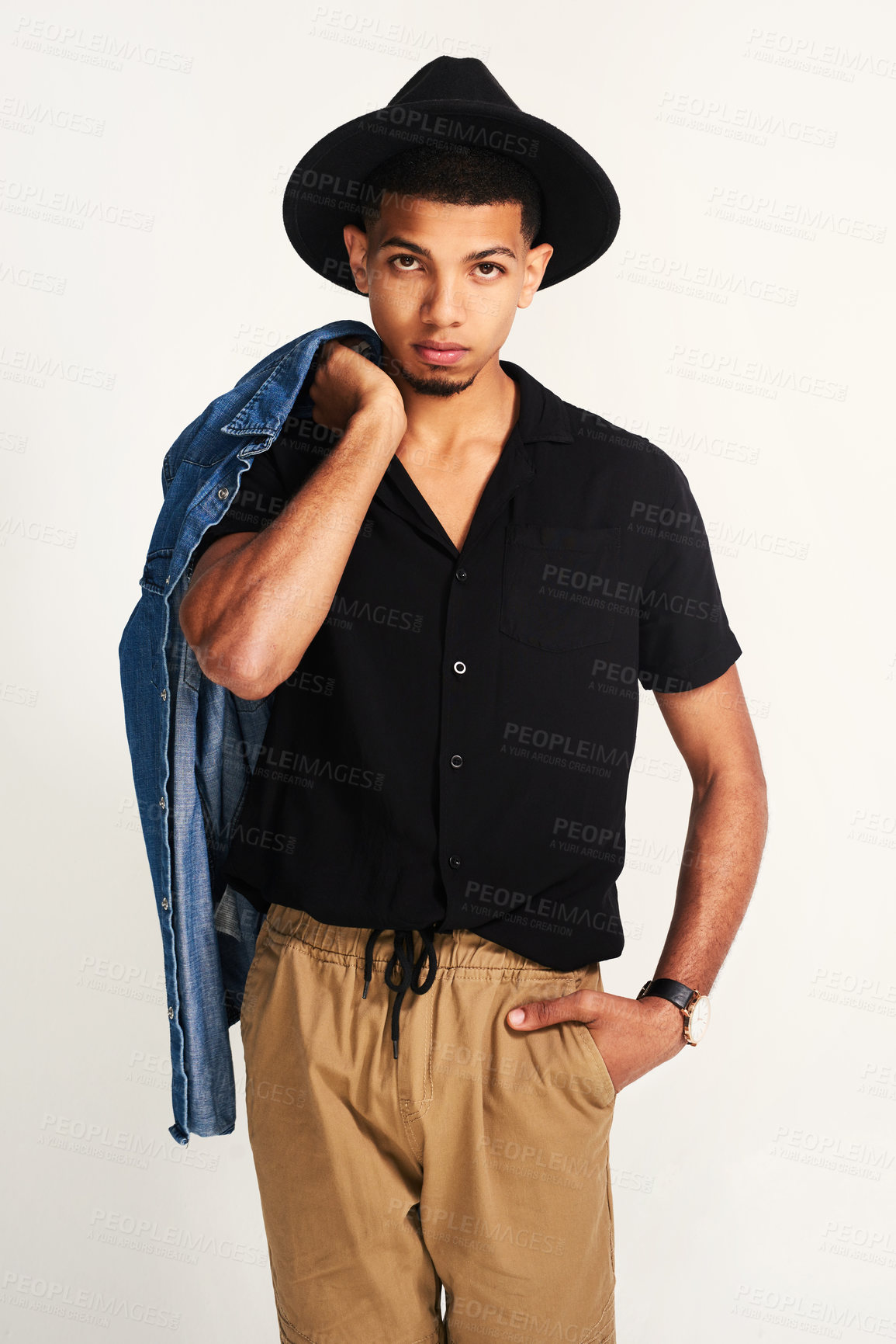 Buy stock photo Portrait of a handsome young man wering a hat and holding a jacket while posing against a grey background