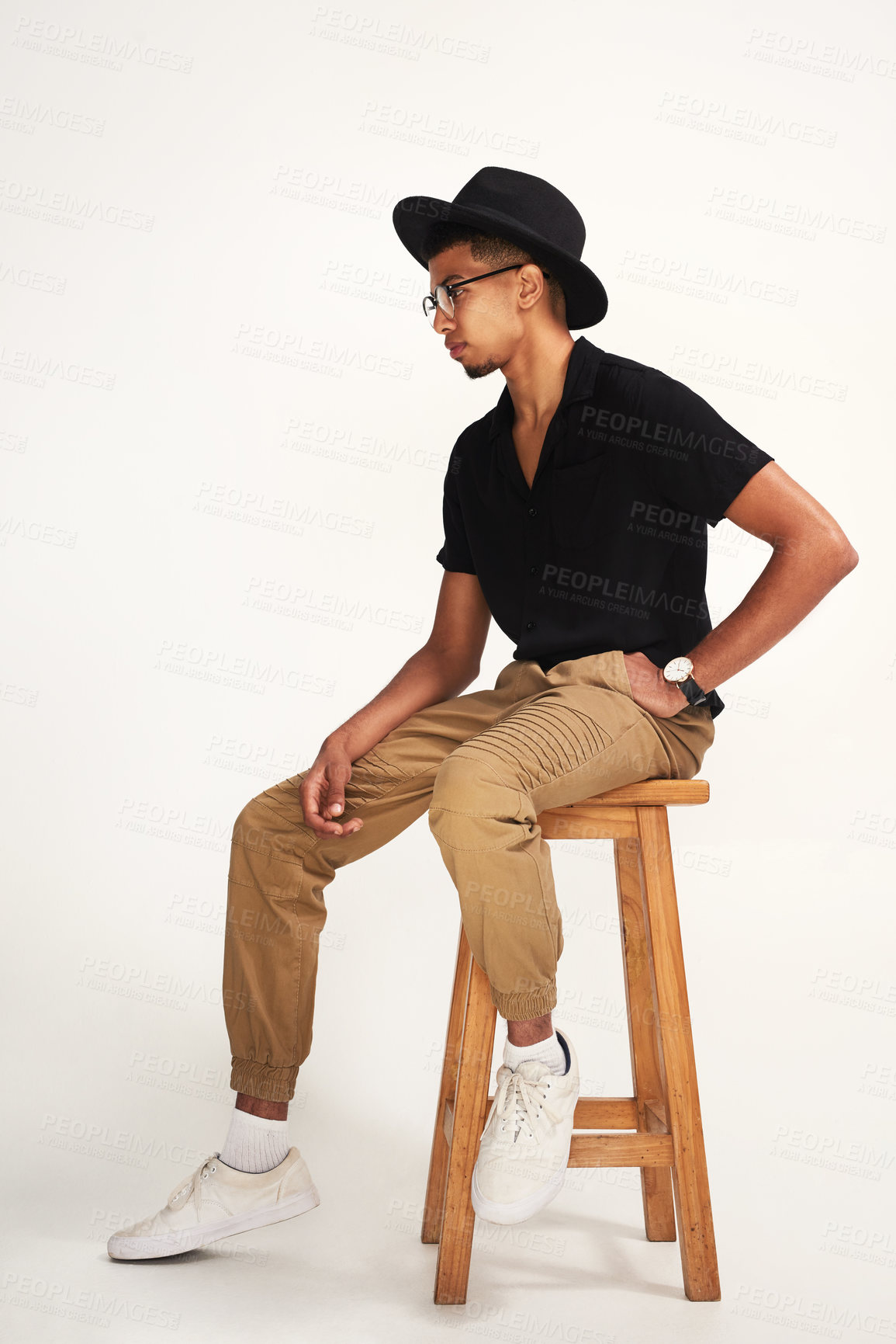 Buy stock photo Studio shot of a handsome young man wearing a hat and glasses while being seated on a chair against a grey background inside of a studio
