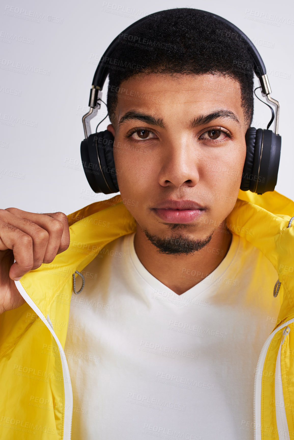 Buy stock photo Portrait of a handsome young man listing to musing on his headphones while standing against a grey background inside of a studio