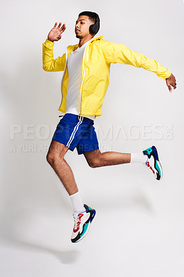 Buy stock photo Studio shot of a handsome young man listening to music while jumping in the air inside of a studio