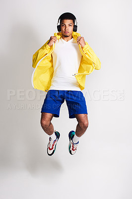 Buy stock photo Portrait of a handsome young man listening to music while jumping in the air inside of a studio