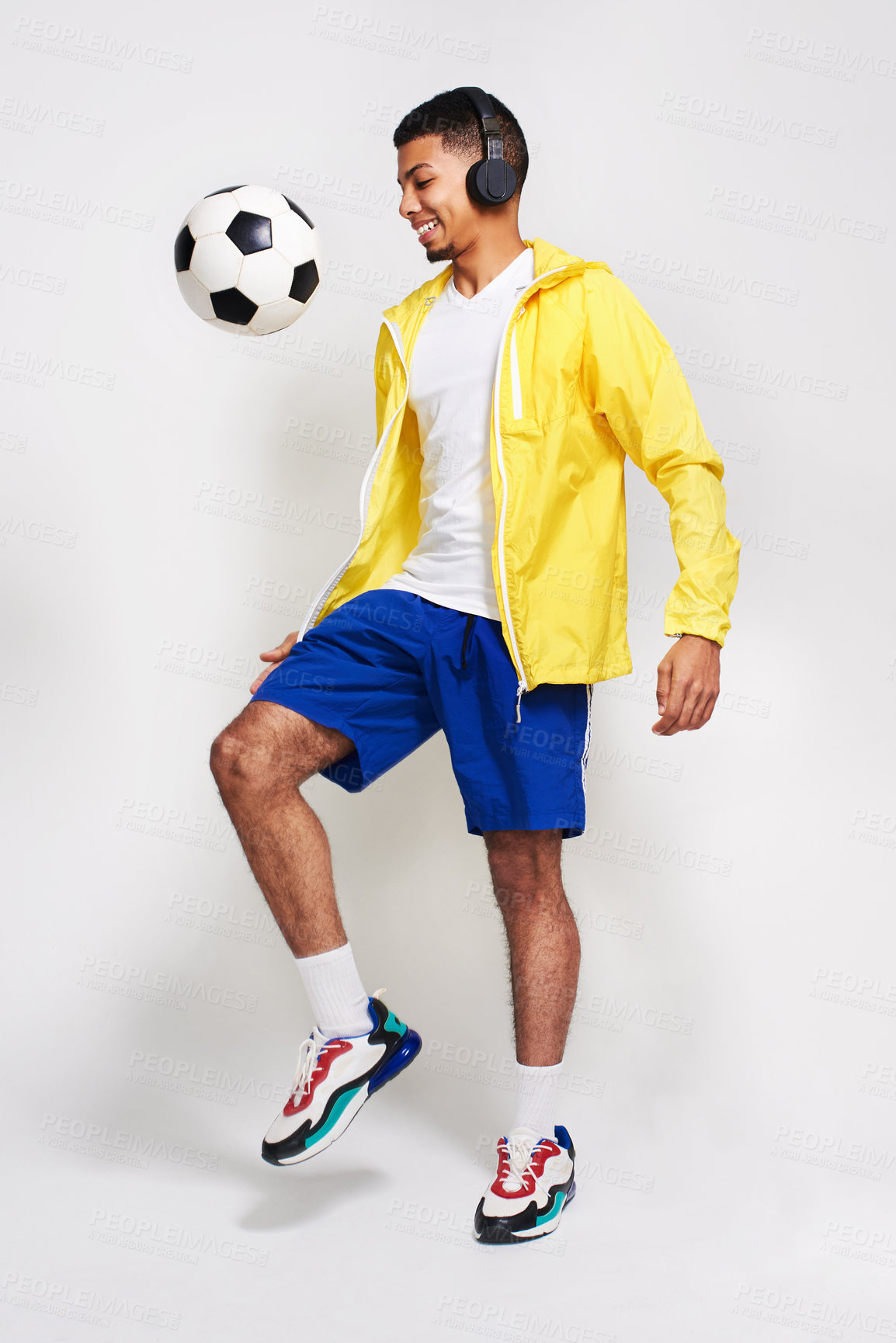 Buy stock photo Studio shot of a handsome young man listening to music while kicking a soccer ball in the air inside of a studio