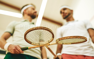 Buy stock photo Cropped shot of two young men crossing their racquets at a squash court