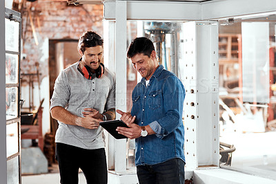 Buy stock photo Cropped shot of two young businessmen using a digital tablet while working together in an office inside their workshop