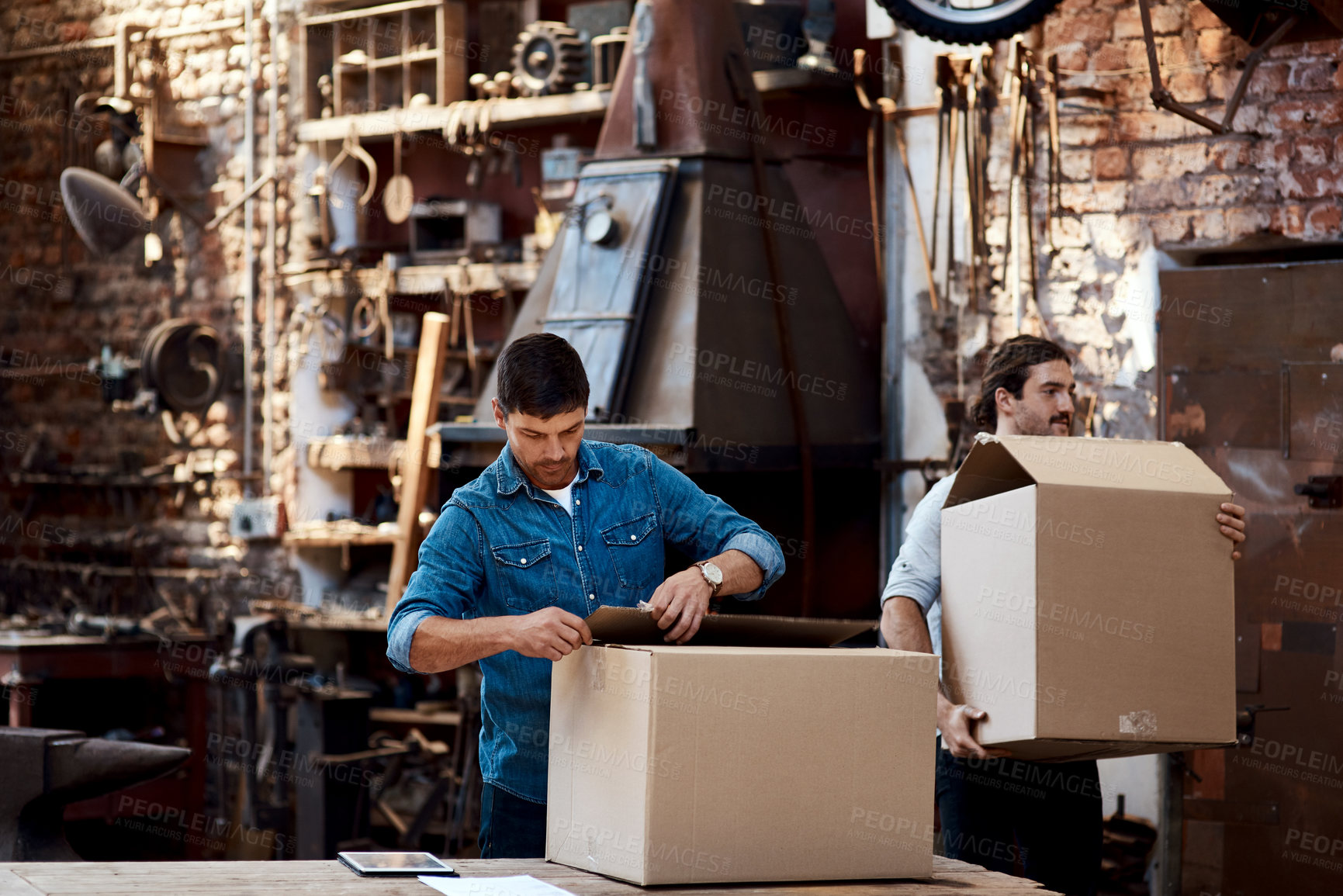 Buy stock photo Cropped shot of two young businessmen carrying boxes while sorting out orders and deliveries inside their workshop