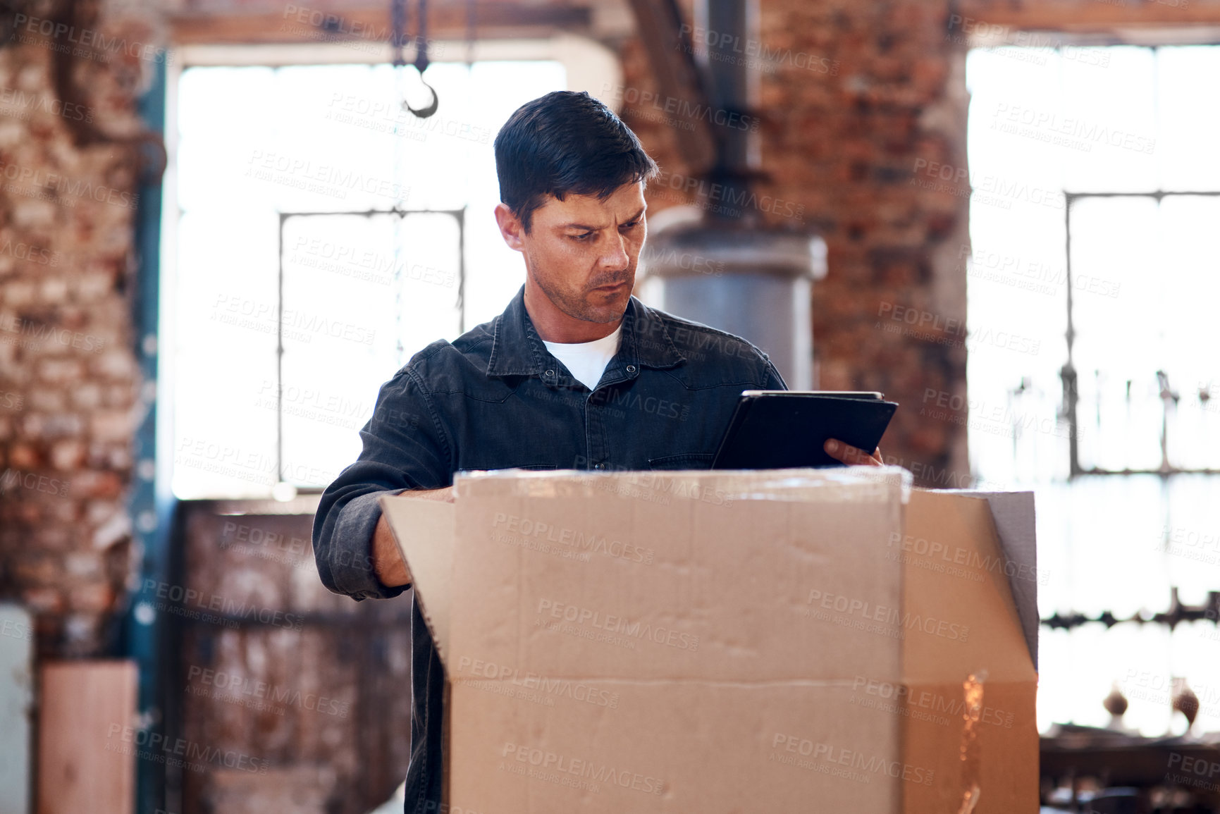 Buy stock photo Cropped shot of a young businessman using a digital tablet while sorting out orders and deliveries inside his workshop