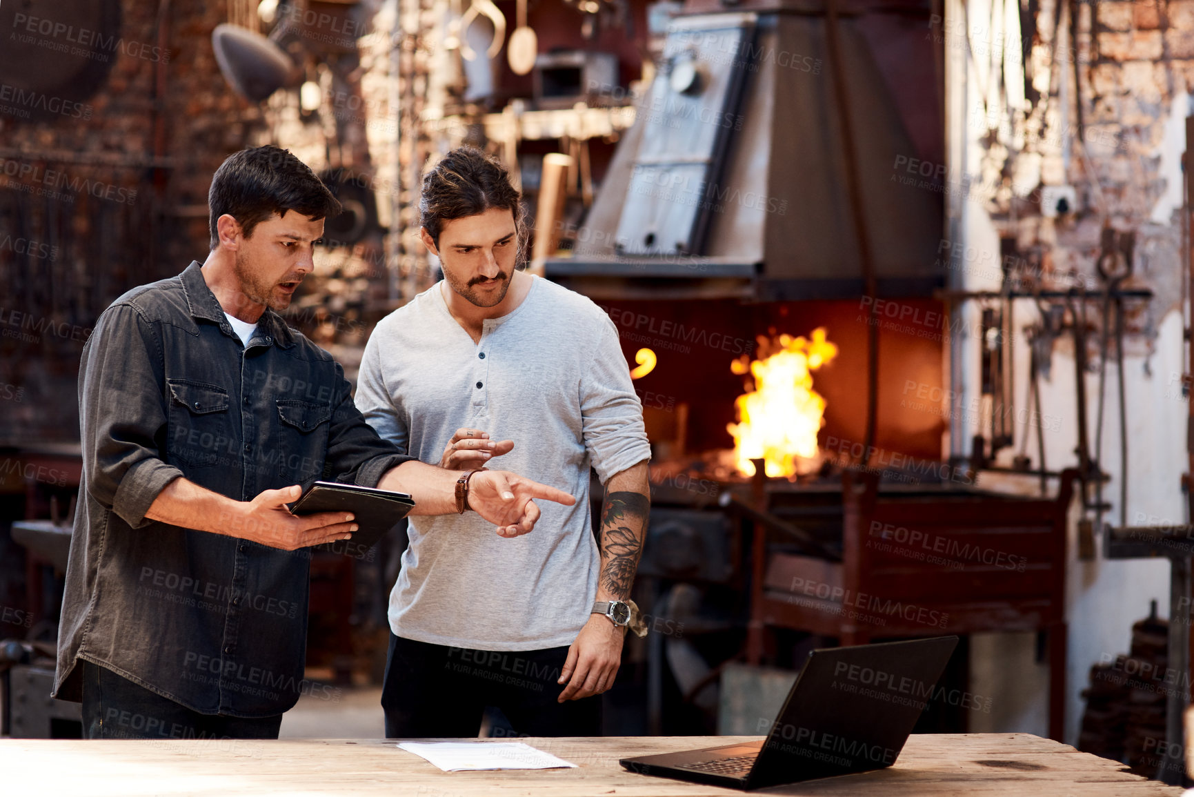 Buy stock photo Cropped shot of two handsome young using their digital devices while working together inside their workshop