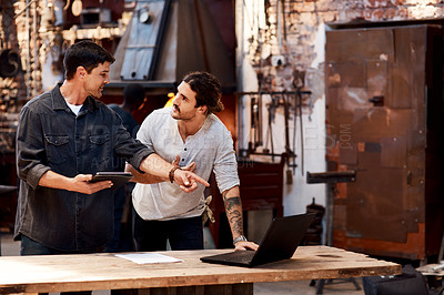 Buy stock photo Cropped shot of two handsome young using their digital devices while working together inside their workshop