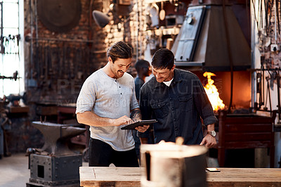 Buy stock photo Cropped shot of two handsome young using a digital tablet while working together inside their workshop