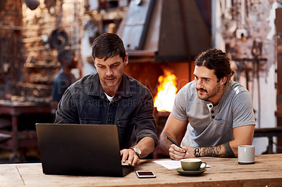 Buy stock photo Cropped shot of two handsome young using a laptop while working together inside their workshop