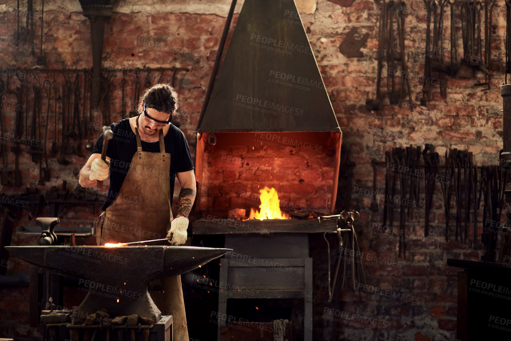 Buy stock photo Blacksmith, forge and man in metal workshop and manual working on hot steel with hammer, sparks and fire. Master, welding job or iron tools manufacturing and expert, trade and dark workspace