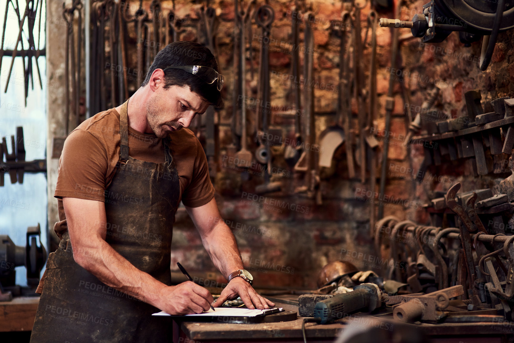 Buy stock photo Cropped shot of a handsome young craftsman filling out paperwork while working inside a metal workshop